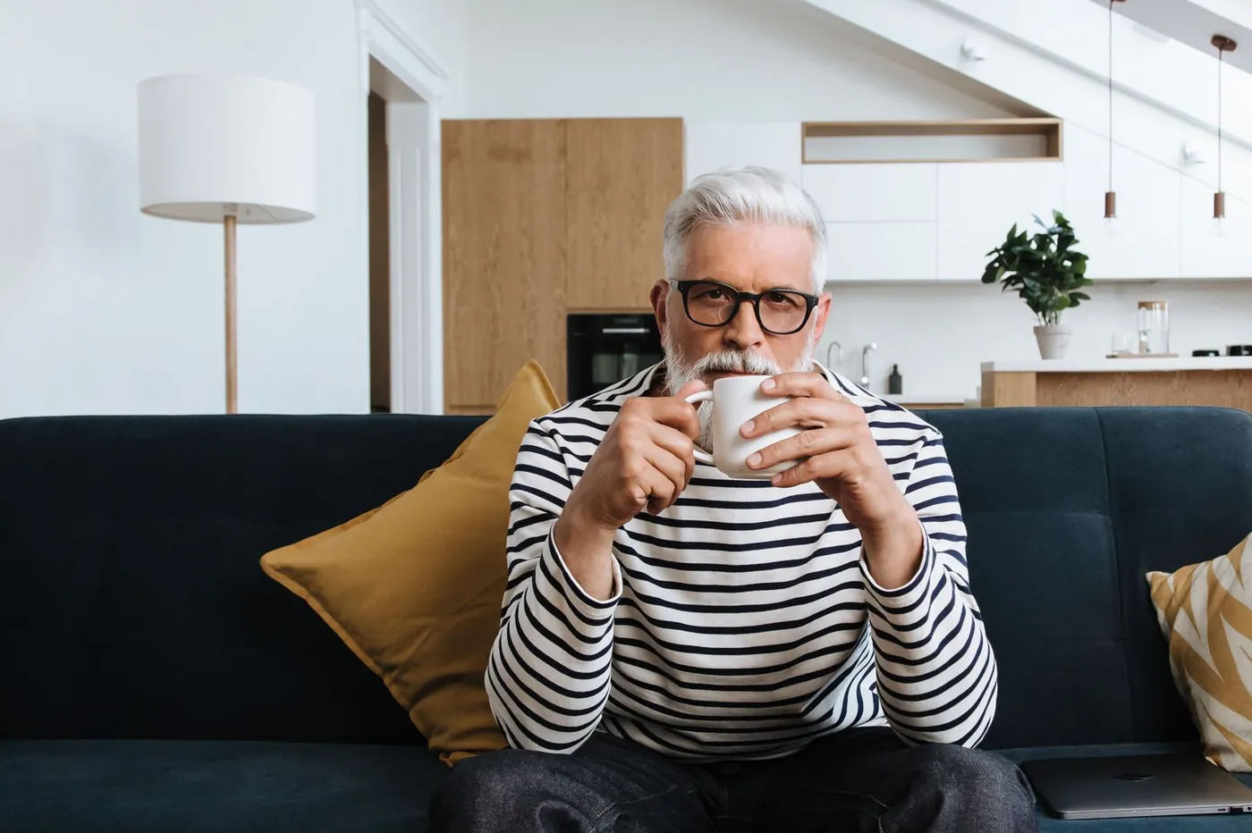 Man met grijs haar drinkt koffie op de bank