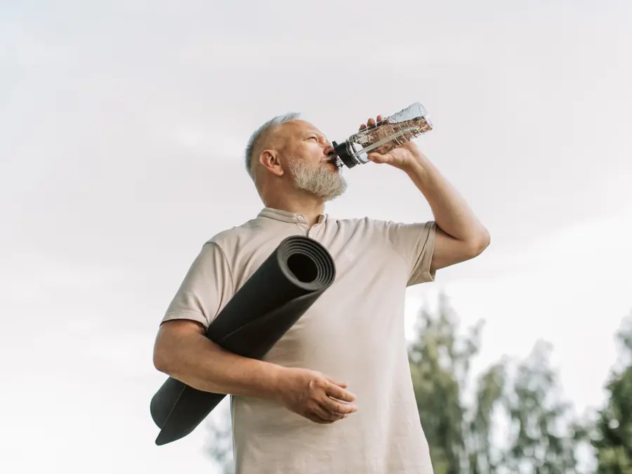 Man met yogamat drinkt water uit een fles